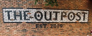 A brick wall with the text "THE OUTPOST EST. 2019" in large, bold letters.