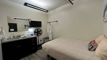 Un dormitorio moderno con cama, mesita de noche, espejo, ventilador y televisor.