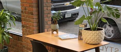 A wooden table with a black chair in front of a brick wall with a window. There are two potted plants on the table.