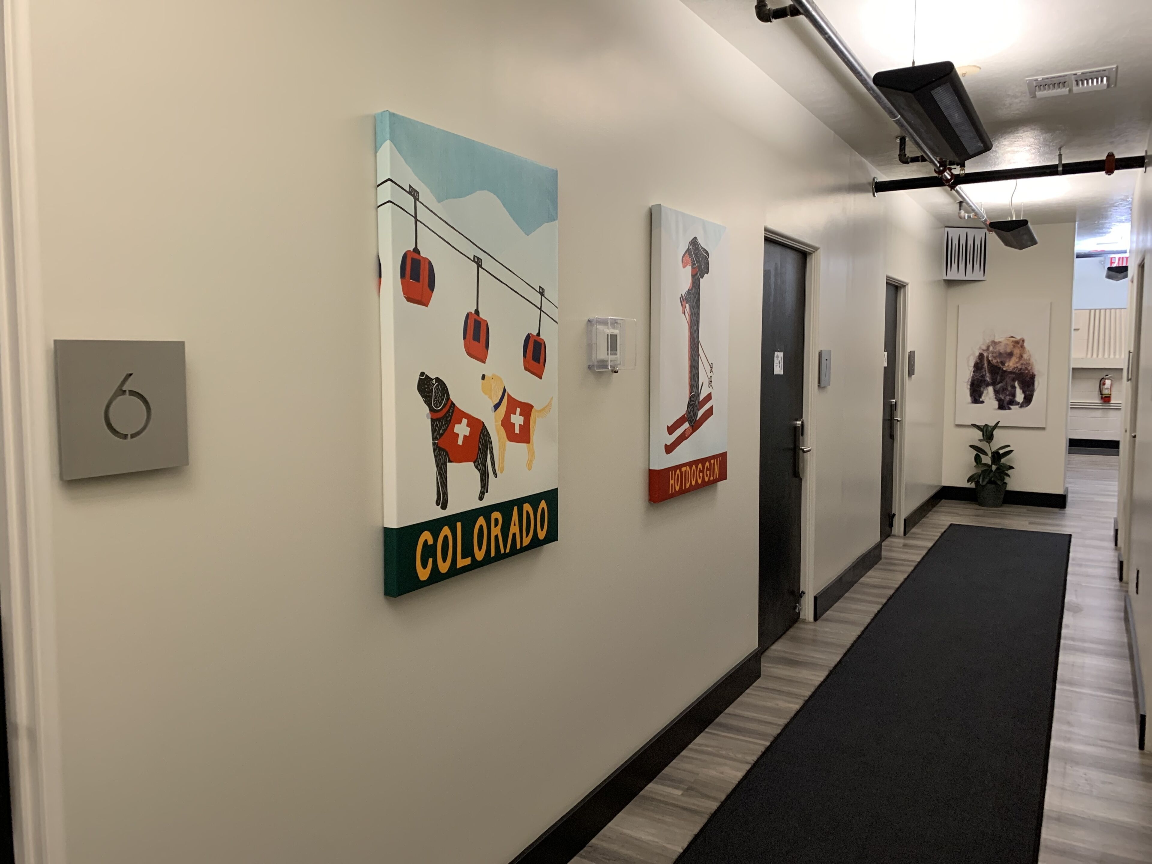 A hallway with artwork depicting dogs and a bear, a fire alarm, and a plant.