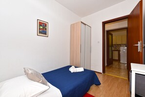 Une chambre à coucher avec un lit, une armoire, une porte donnant sur la cuisine et un tableau encadré au mur.