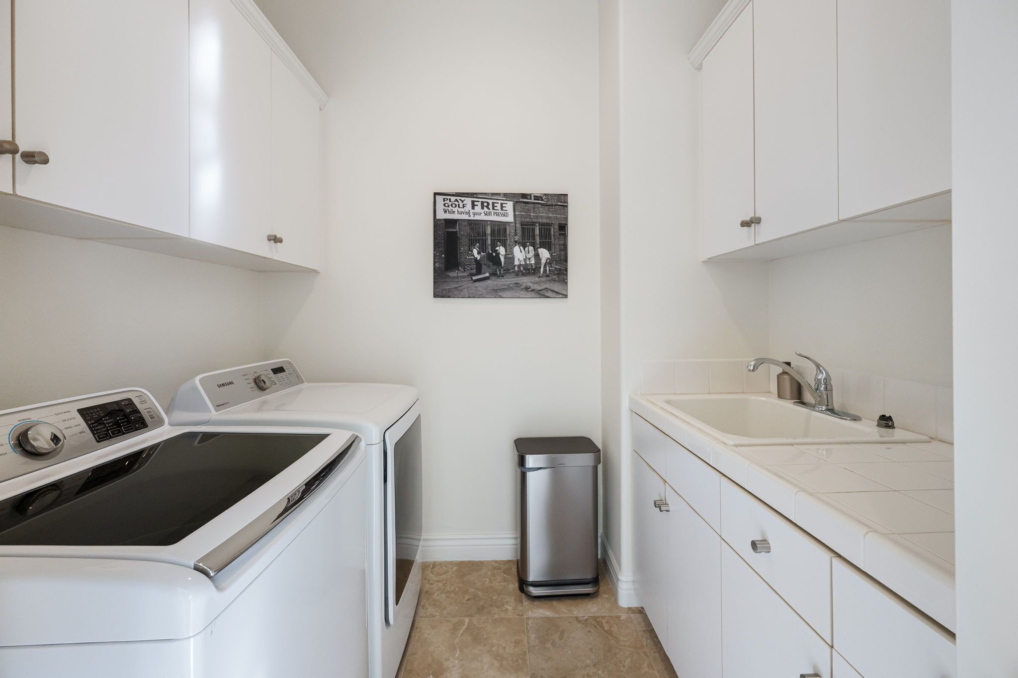A laundry room with a washing machine, dryer, sink, and trash can.