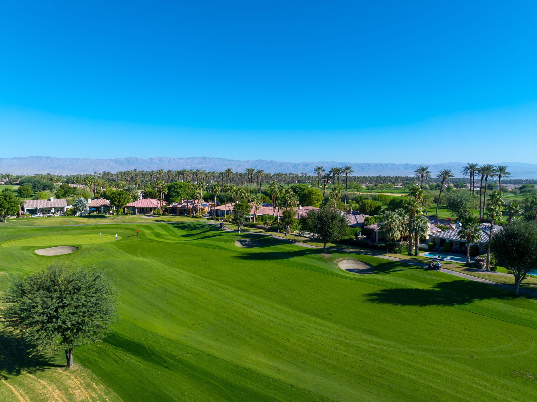 A golf course with a clear view of the fairway, sand bunkers, and a clubhouse.