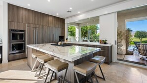 A modern kitchen with a large island, bar stools, built-in ovens, and a view of the outdoor patio. - PGA West #11 - 3 bedroom Pool Home -Weiskopf, LQ permit #111254 (La Quinta)