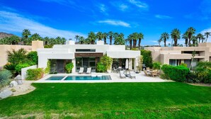 Una casa moderna de dos pisos con piscina, mobiliario exterior y palmeras.