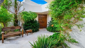 Un patio con un banco de madera, una puerta y abundante vegetación.