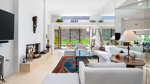 Amplia sala de estar con un sofá grande, una mesa de centro y una chimenea. Una ventana grande ofrece vistas al exterior.