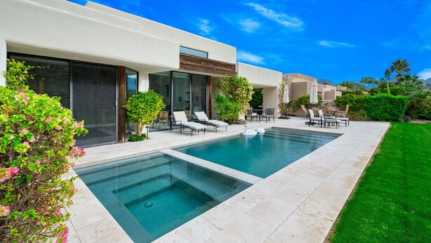 Una casa moderna con piscina, mobiliario exterior y un césped bien cuidado.
