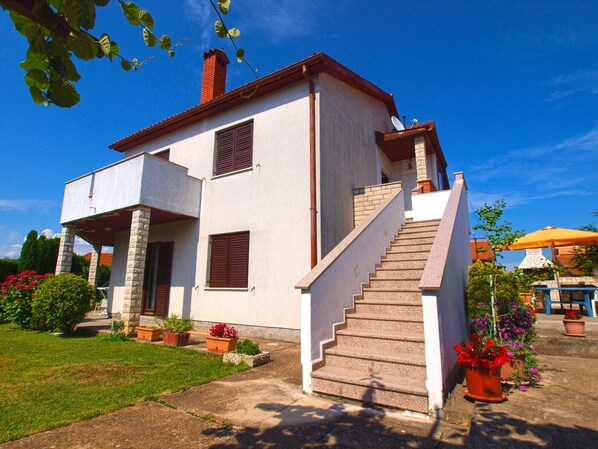 A two-story house with a staircase leading to the entrance, surrounded by potted plants and a clear blue sky. - Apartment 39/50 (Istria - Banjole), 500m from the beach (Banjole)