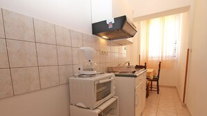 A compact kitchen with a microwave, oven, and a small refrigerator. There is a window with curtains and a chair in the dining area. - Apartment 39/52 (Istria - Banjole), 500m from the beach (Banjole)