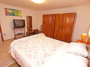 A bedroom with a bed, wooden wardrobe, a television on a stand, and a painting on the wall.