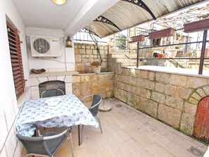 A patio area with a table and chairs, a wall-mounted air conditioning unit, and a stone wall with a window and a metal gate.