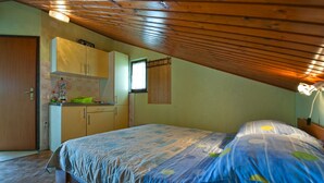 A bedroom with a sloped ceiling, a bed with patterned bedding, a small kitchenette, and a window with curtains. - Apartment 41/23324 (Istria - Stinjan), 700m from the beach (Stinjan)