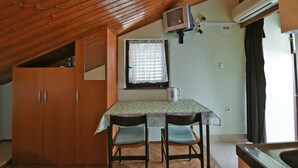 A small kitchen with wooden cabinets, a table with two chairs, a window with curtains, and an air conditioning unit. - Apartment 41/23324 (Istria - Stinjan), 700m from the beach (Stinjan)