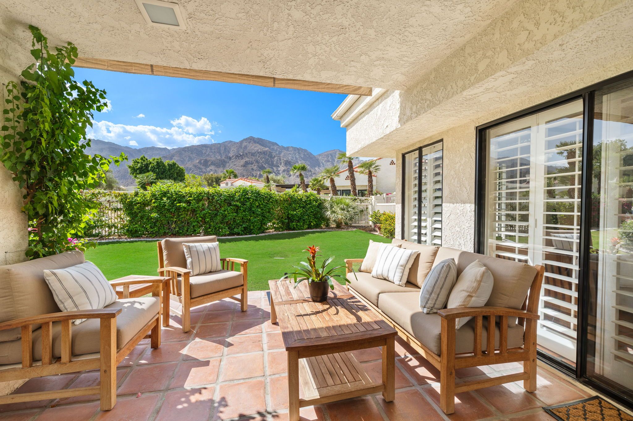An outdoor patio with a view of mountains, a lawn, and a pool.