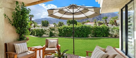 A patio with a wooden table and chairs, a beige sofa, and a large umbrella.
