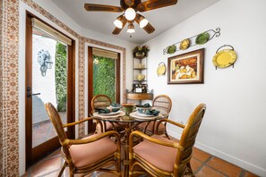 Zona pranzo con tavolo in vetro, sedie in vimini e ventilatore a soffitto.