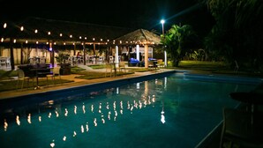 A poolside area with lounge chairs and a covered seating area, surrounded by greenery.