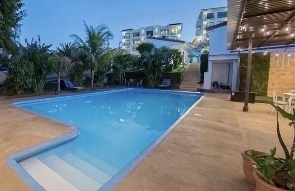 Una piscina de borde curvo, rodeada por una terraza de hormigón y macetas con plantas.