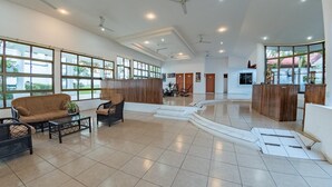 A spacious lobby with a brown sofa, black chairs, and a coffee table. There are multiple doors and a reception desk.