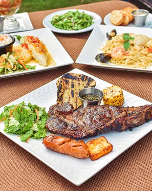 Una mesa de comedor con una variedad de platos, incluyendo carne a la parrilla, verduras y pasta.