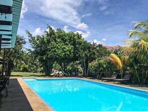 Piscina rodeada de vegetación exuberante y palmeras, con un cielo azul despejado.