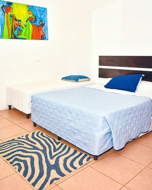 Un dormitorio con cama, una mesita de noche pequeña, un cojín azul, un tapete con estampado de cebra y un cuadro de colores en la pared.