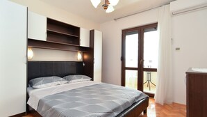 Une chambre à coucher avec un lit, des étagères intégrées, un luminaire au plafond et une vue sur l’extérieur, visible à travers une porte.