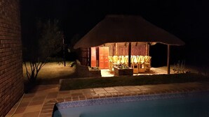 A nighttime view of a pool area with a covered seating area and a brick wall. - Tata Farm Game Lodge (Hammanskraal)