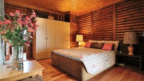 A wooden cabin bedroom with a bed, bedside lamps, a wooden wardrobe, and a vase with flowers on a table. - Tata Farm Game Lodge (Hammanskraal)