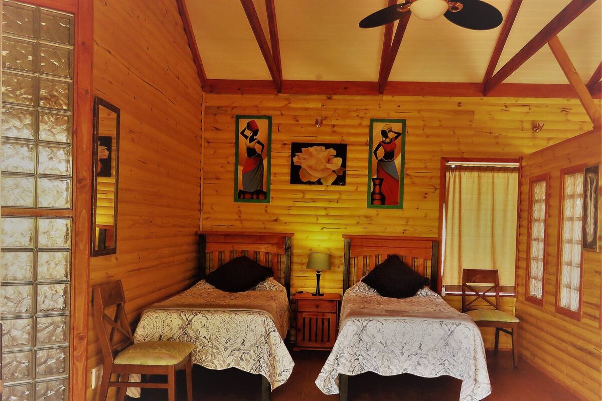 A wooden cabin room with two beds, a ceiling fan, and wooden walls.