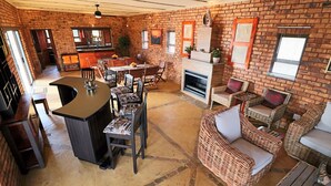A spacious living area with a bar, dining table, and wicker furniture. - Tata Farm Game Lodge (Hammanskraal)