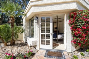 Une maison à l’extérieur blanc, dotée d’un patio couvert, d’une porte avec un panneau de verre et d’un petit jardin agrémenté de rochers et de plantes.