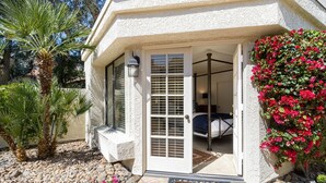 Une maison à l’extérieur blanc, dotée d’un patio couvert, d’une porte avec un panneau de verre et d’un petit jardin agrémenté de rochers et de plantes.