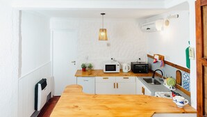 Una cocina compacta con armarios blancos, encimera de madera, microondas, hervidor y una lámpara colgante.