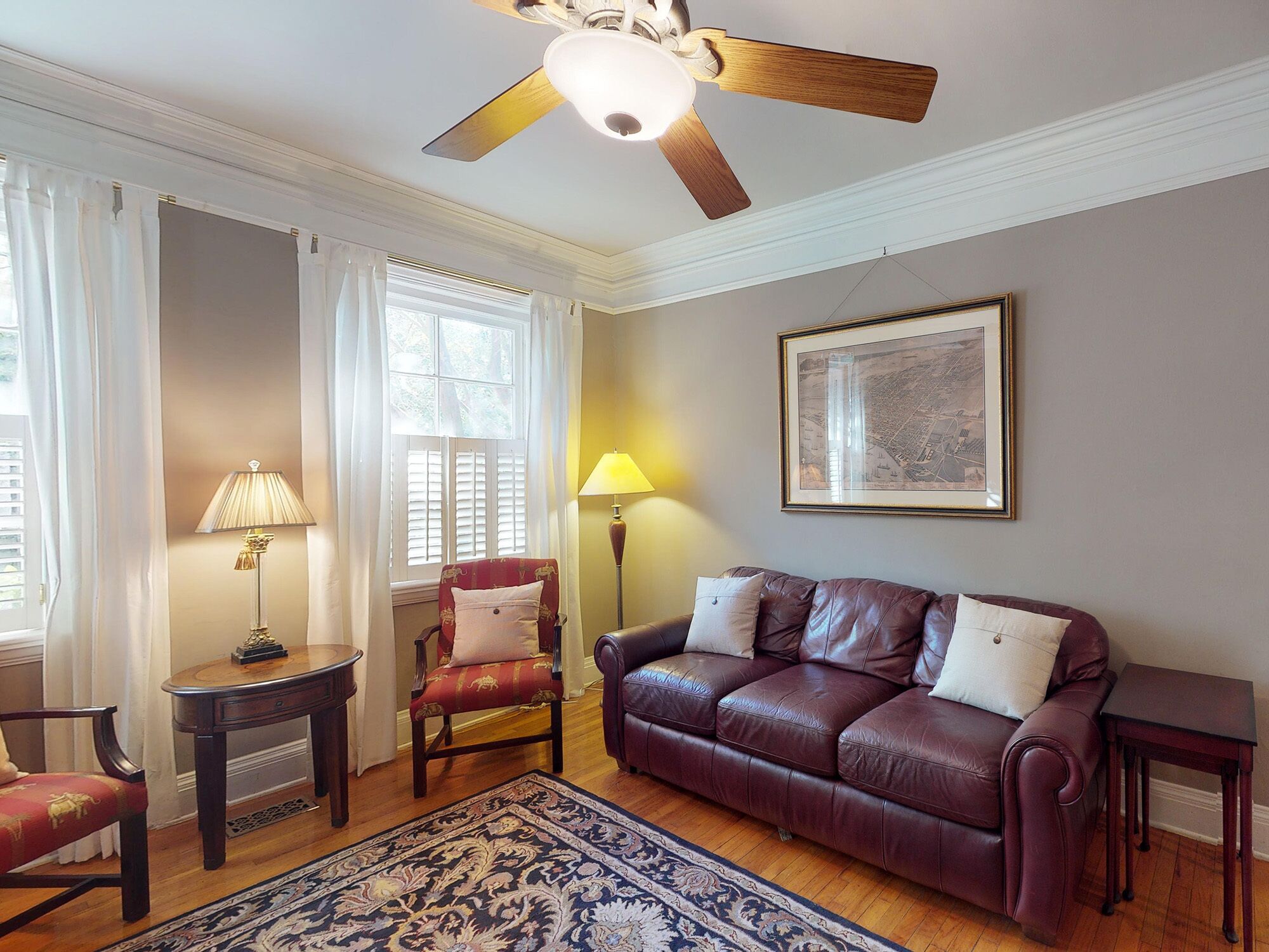 A living room with a leather sofa, a red armchair, a small table, a floor lamp, and a ceiling fan.