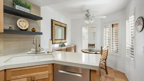 A modern kitchen with a white countertop, wooden cabinets, and a built-in oven. There is a dining area with a table and chairs, and a ceiling fan above. - Santa Rosa Cove #14 Mtn. Views, 2 bed/2 bath Pet friendly Home, Permit 068343 (La Quinta)