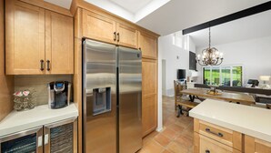 A modern kitchen with wooden cabinets, a stainless steel refrigerator, a coffee maker, and a dining area with a bench. - Santa Rosa Cove #14 Mtn. Views, 2 bed/2 bath Pet friendly Home, Permit 068343 (La Quinta)