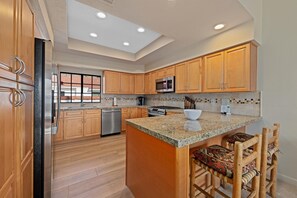 A modern kitchen with wooden cabinets, stainless steel appliances, and a large island with bar stools.