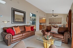 A living room with two brown leather sofas, a glass coffee table, and a large mirror on the wall.