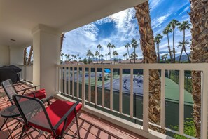 A balcony with a view of a tennis court, palm trees, and a clear sky.