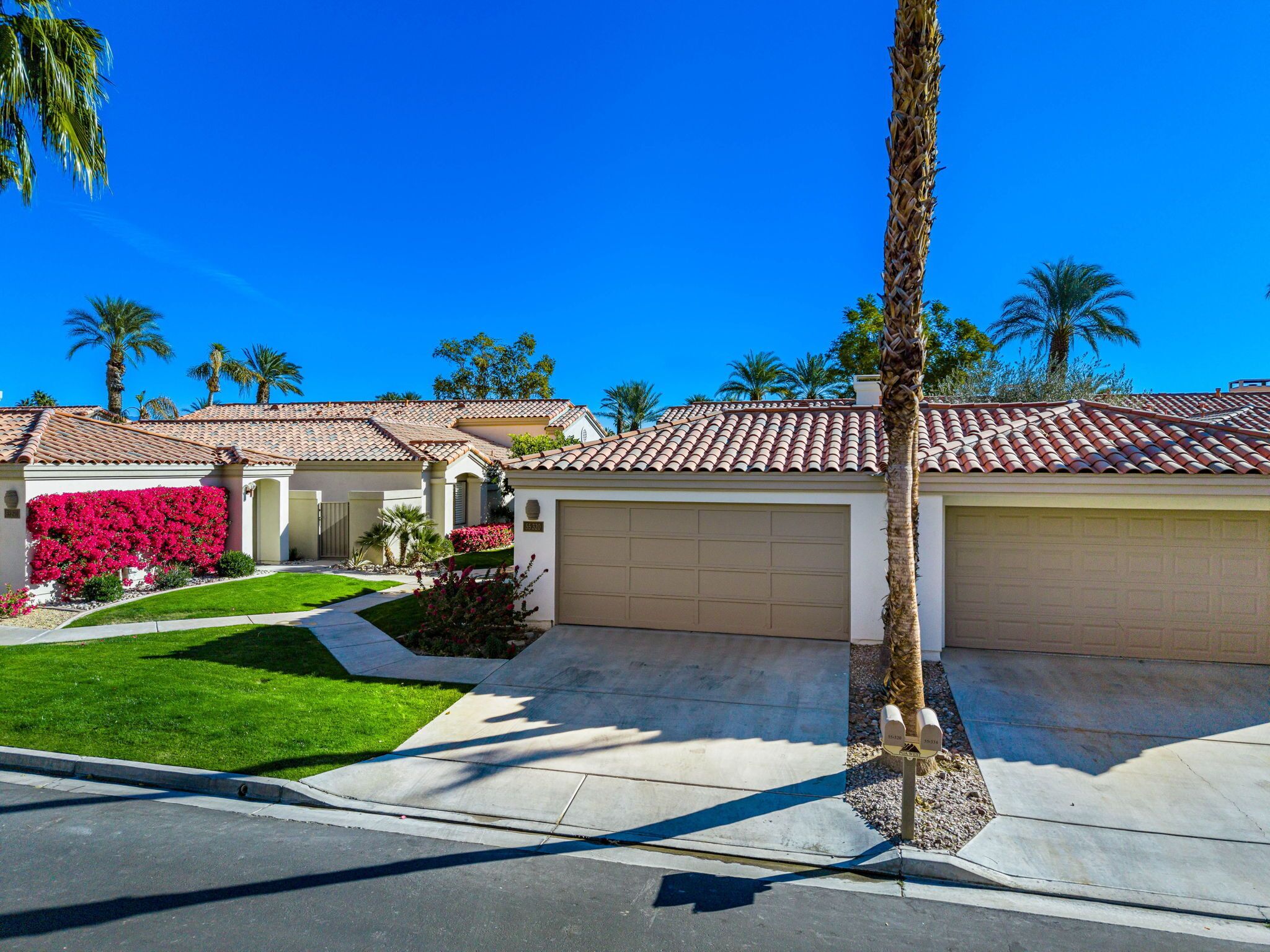 A residential area with houses featuring red-tiled roofs, a well-maintained lawn, and palm trees.