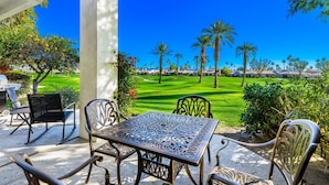 An outdoor patio with a table and chairs, overlooking a well-manicured lawn and palm trees.