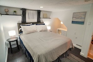 Une chambre à coucher avec un grand lit, des tables de chevet avec des lampes, un ventilateur de plafond, une étagère avec des objets décoratifs et un tableau au mur.