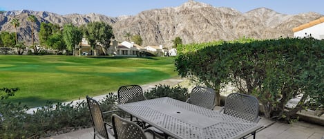 A patio area with a table and chairs, a view of a golf course, and mountains in the background.