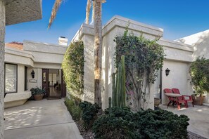 A courtyard with a white building, a palm tree, and red chairs.