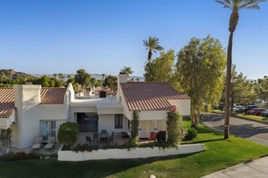 A two-story house with a tiled roof, a patio with outdoor furniture, and a well-maintained lawn.