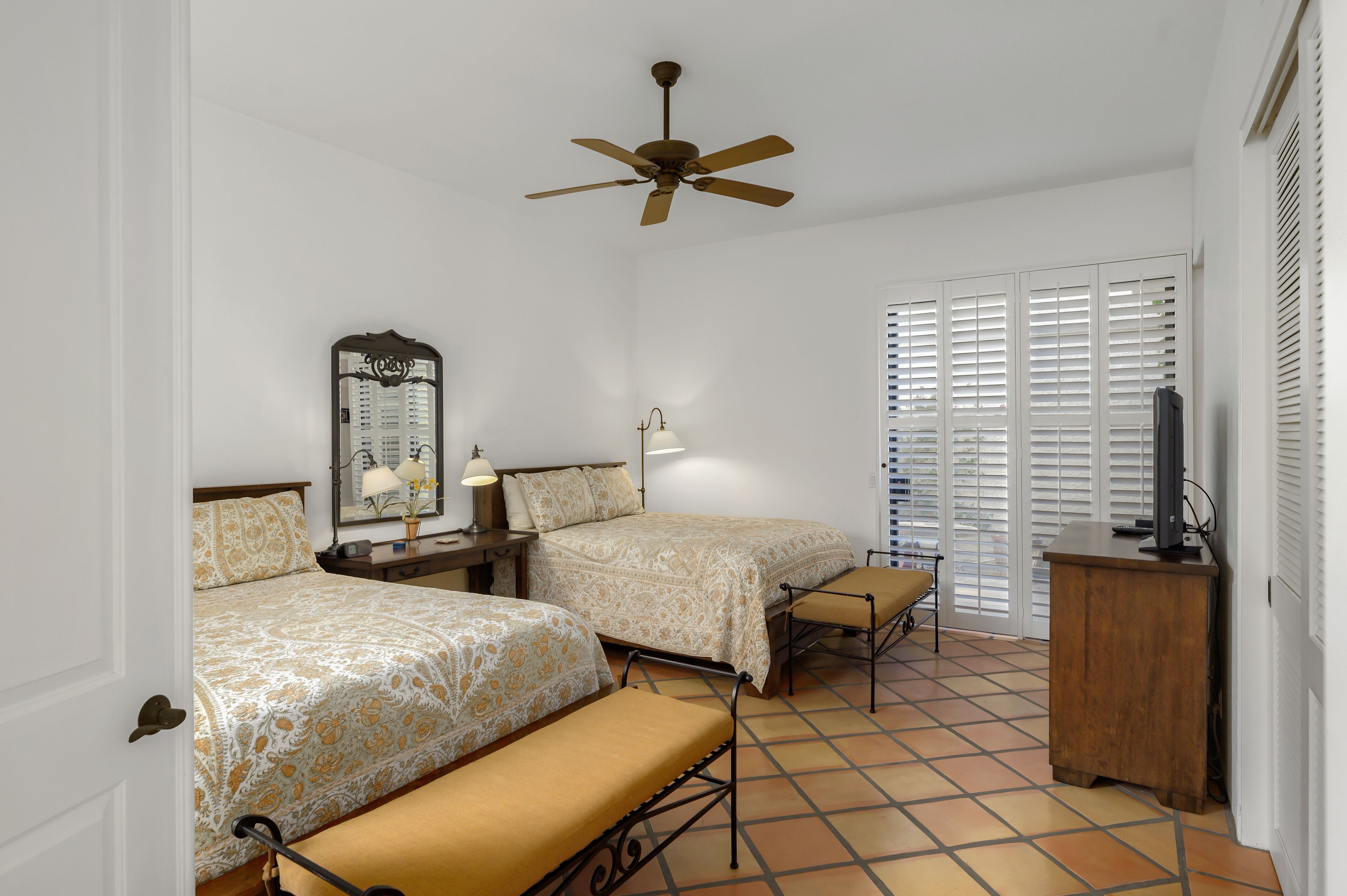 A hotel room with two beds, a ceiling fan, a TV, and a large window with blinds.