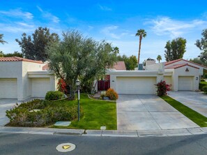 A residential area with two houses, each with a garage, surrounded by well-maintained lawns and various plants.