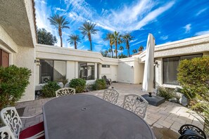 A patio area with a table and chairs, surrounded by palm trees and a clear blue sky.